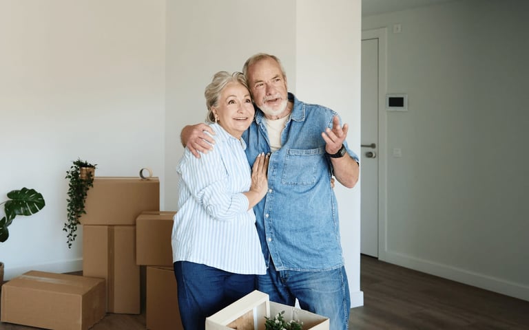 Senior couple embracing in new home with cardboard boxes and potted plant.