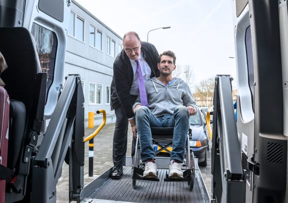 Man being assisted into a van using a wheelchair lift.