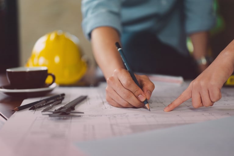 Two people reviewing blueprints with drafting tools and a hard hat nearby.