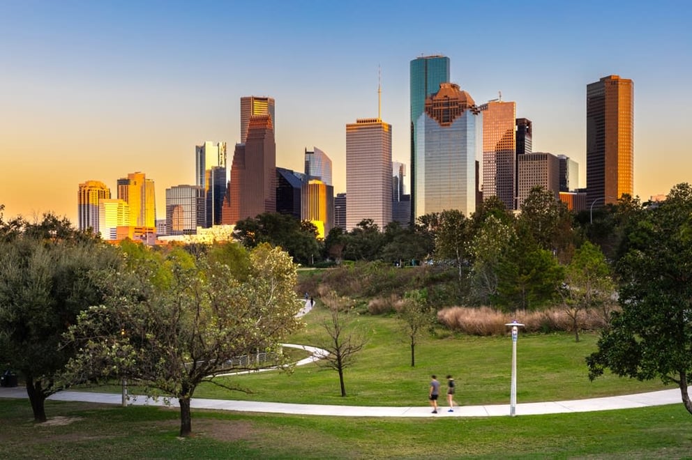 Two people walking on a path in a park with a city skyline at sunset.