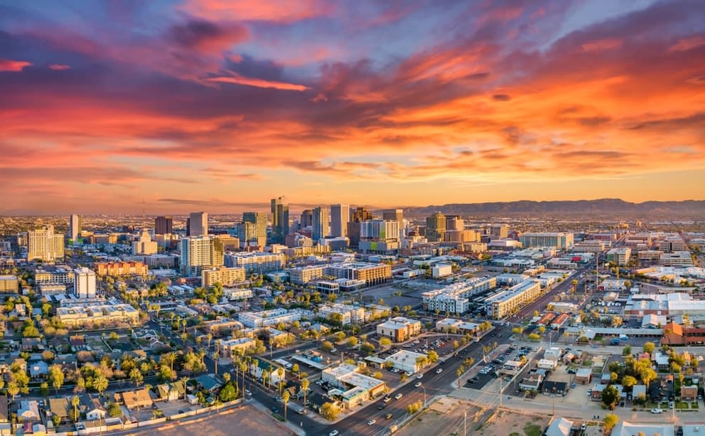 Aerial view of a city skyline at sunset with warm clouds and distant mountains.