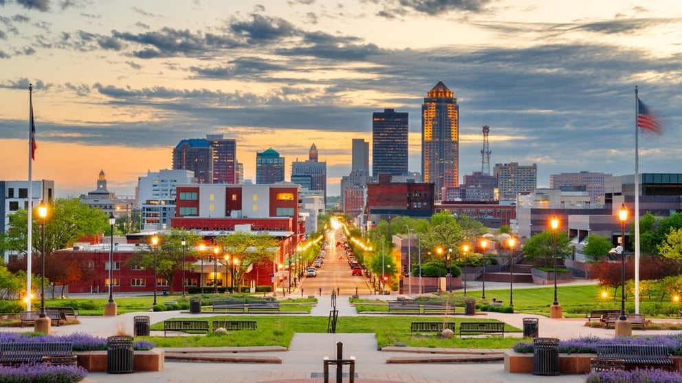 City skyline at dusk viewed from a park pathway with illuminated streetlights.