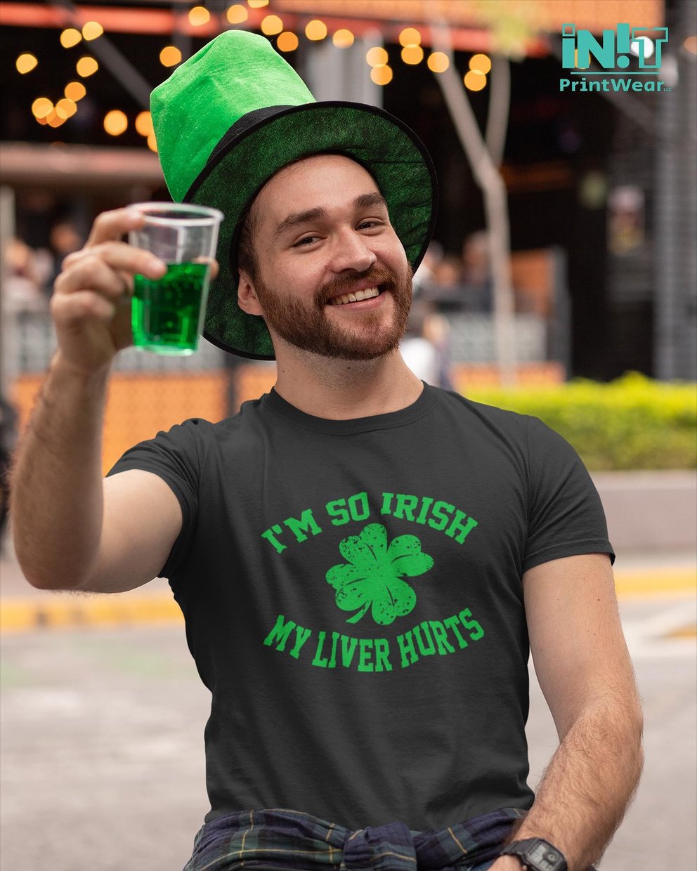 Man in green hat and shirt toasting with green drink outdoors.