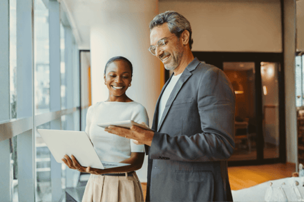 Two professionals collaborate on a laptop near a window in a modern office.