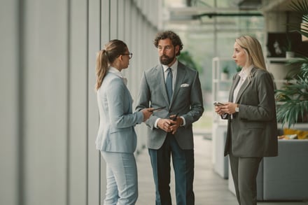Three professionals in business attire conversing in a modern office corridor.