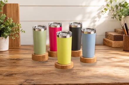 Four colorful insulated tumblers on wooden coasters on a rustic wood table.