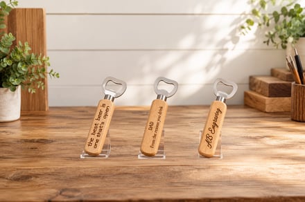 Three wooden bottle openers with engraved messages displayed on clear stands.