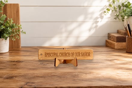 Wooden church sign on a rustic desk with plants and stacked wood blocks.
