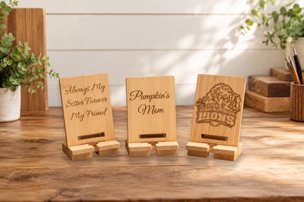 Three wooden phone stands with engraved messages and logos on a rustic table.