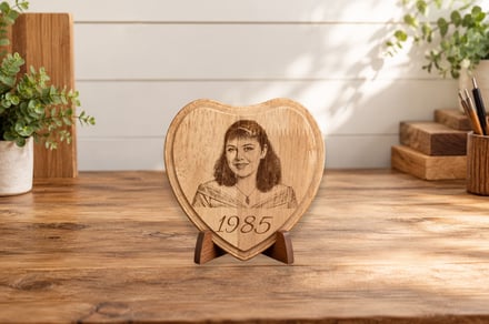 Heart-shaped wooden plaque with engraved portrait and year 1985 on desk.