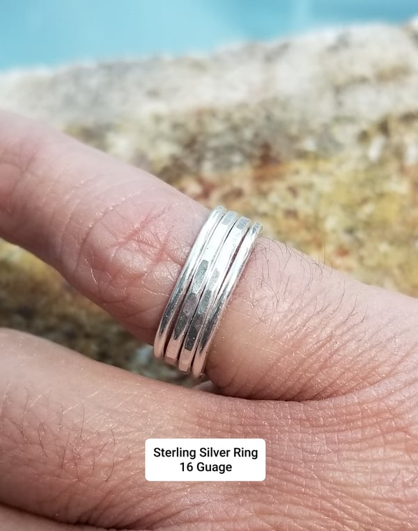 A hand wearing a stack of silver rings near a pool edge.