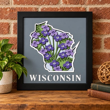 Wisconsin state outline art with purple flowers in a black frame on a wooden shelf.