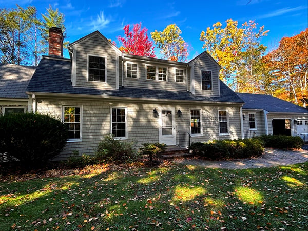 A classic colonial-style house with gray shingles and white trim under a clear blue sky.