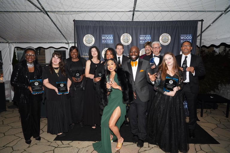 Group of formally dressed people posing with awards at an event under a tent.