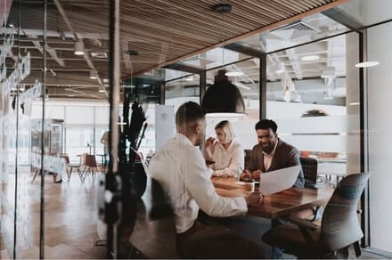 Three professionals collaborate over documents at a wooden table in a modern office.
