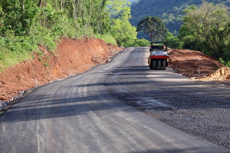 Road roller compacting new asphalt on a winding mountain road.