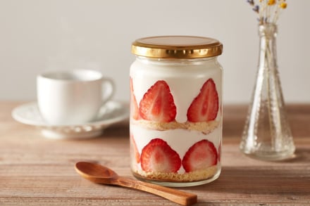 A layered strawberry yogurt dessert in a glass jar on a wooden table.