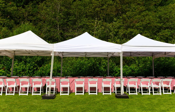 Rows of white chairs under canopy tents on a grassy field.