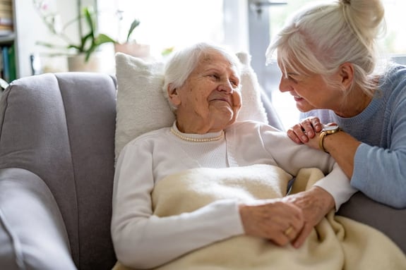 Two women with white hair share a tender moment on a couch.