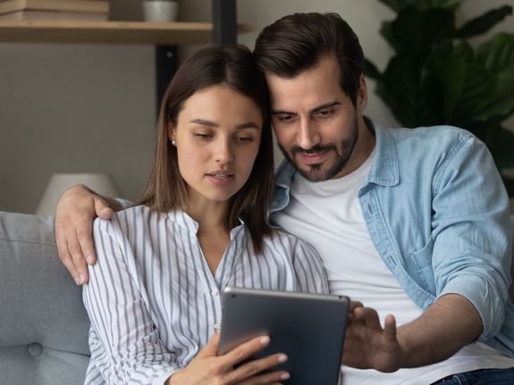 Couple reviewing content on a tablet while seated together on a sofa.