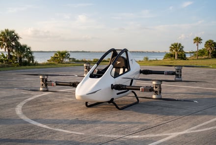 A white electric vertical takeoff and landing vehicle on a paved helipad near water.