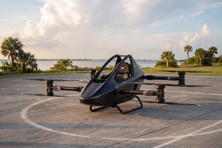 A sleek black electric vertical takeoff and landing aircraft on a paved helipad.