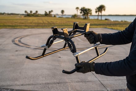 Person holding a metal bike rack frame outdoors near water.
