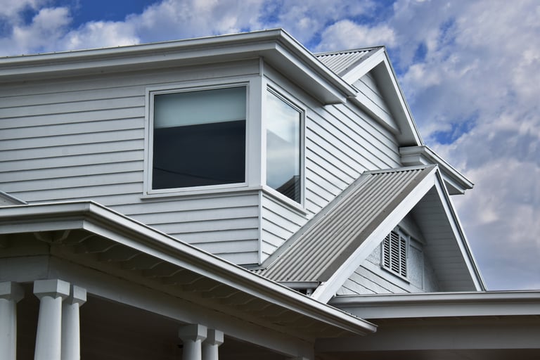 ROOFLINE WITH VARIOUS MULTI ANGLED GABLED CORREGATED IRON ROOFING with gutters, flat patio verandah roof thick columns on a large architectural white wooden siding weatherboard character style house
