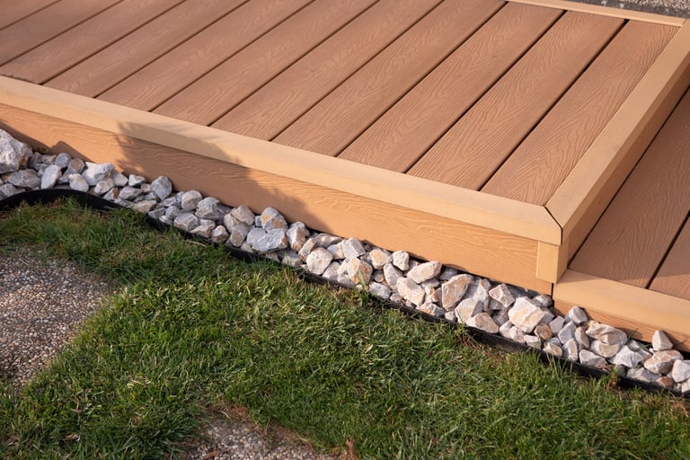 Composite WPC terrace decking with step and corner trim, garden walkway detail with grass and decorative stones, close-up.
