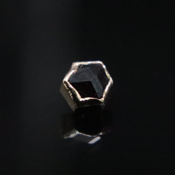 A hexagonal black gemstone set in a textured silver bezel on a reflective surface.