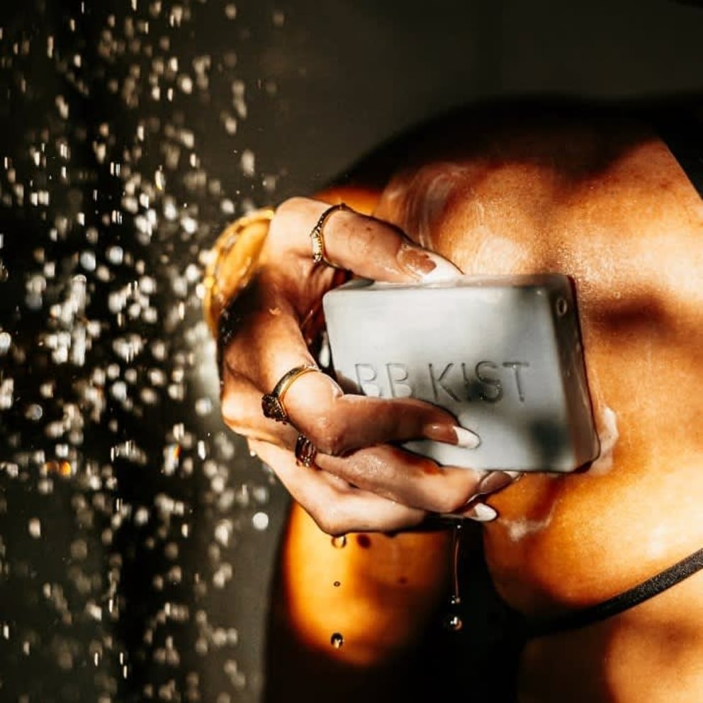 A hand holds a bar of soap under falling water droplets.
