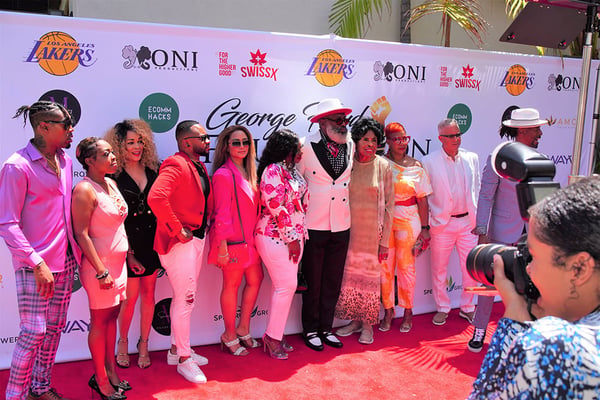 Group of diverse people posing on a red carpet at a branded event.