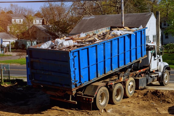 Large roll-off dumpster truck hauling construction waste from jobsite.