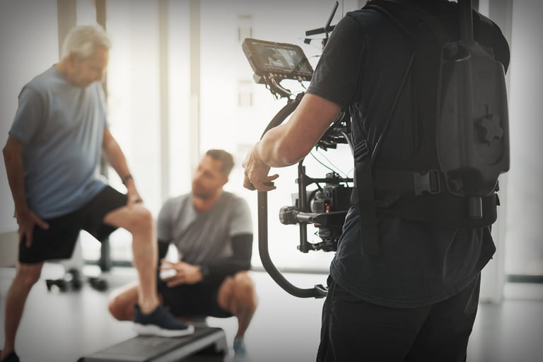 Cinematographer filming two men exercising in a bright studio.