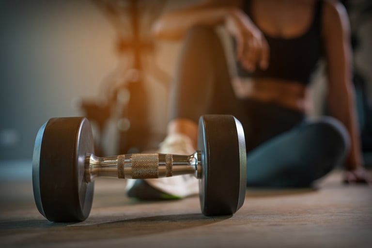 A dumbbell in focus with a person resting in the background.