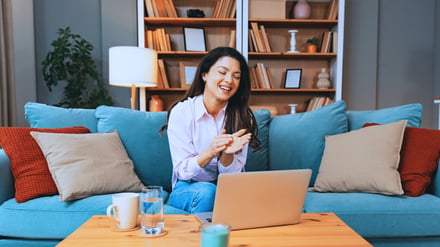 Woman laughing while working on laptop at home.