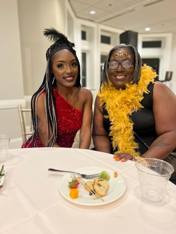 Two women in festive attire smiling at a formal dinner table.