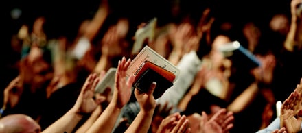 Crowd of people clapping with hands raised in a dimly lit venue.