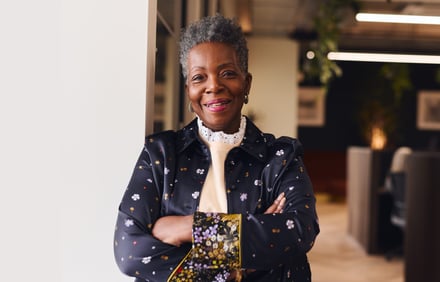 A smiling woman with short grey hair stands confidently with arms crossed in a modern office.