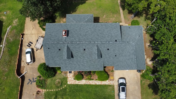 Aerial view of a single-story house with gray shingle roof and two parked cars.