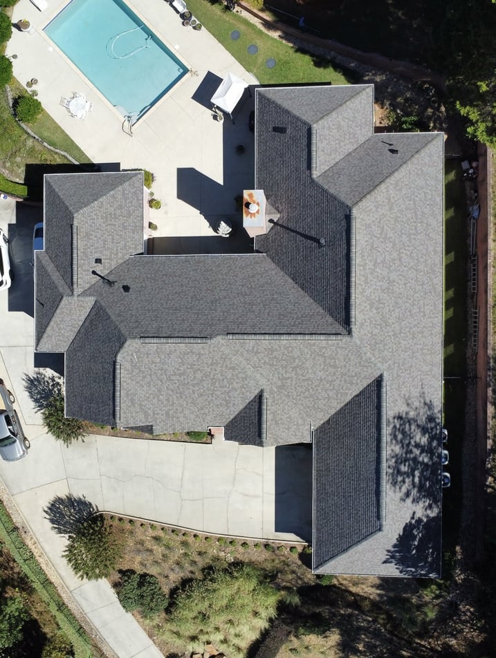 Aerial view of a modern single-family home with gray shingle roof and backyard pool.