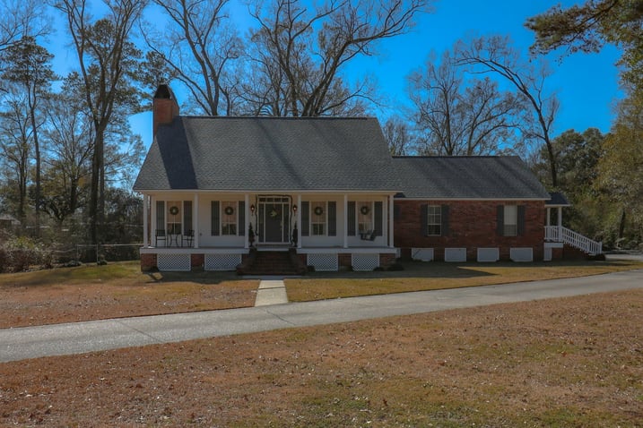 A modest single-story house with a front porch and brick siding under a clear blue sky.