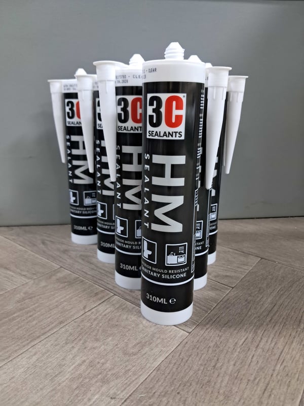 Six tubes of 3C HM sealant arranged upright on a wooden floor.