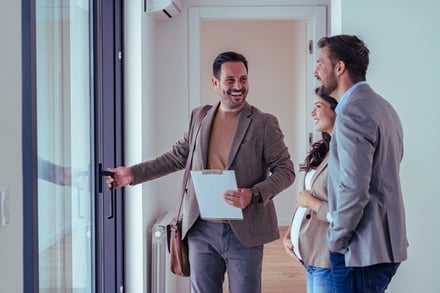 Three people smiling at a glass door in a modern home.