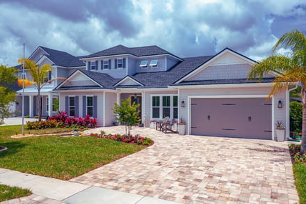 Modern two-story house with gray shingles and stone accents under dramatic clouds.