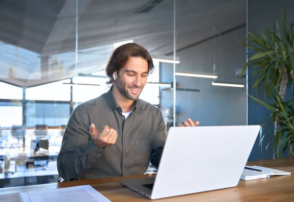 Man celebrating a win while working on a laptop in a modern office.