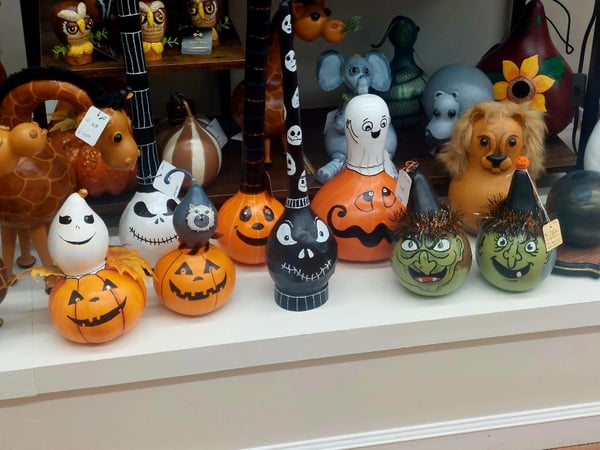 A row of painted gourds shaped like Halloween characters on a white shelf.