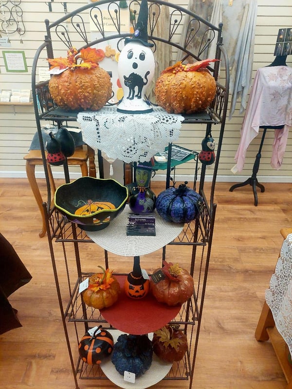 A black metal tiered stand displays Halloween-themed pumpkins and decorations in a retail setting.