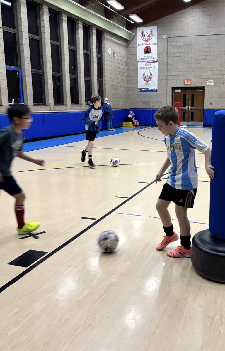 Boys playing soccer indoors on a polished wooden court.