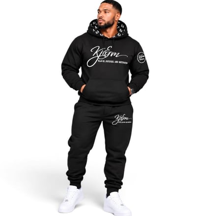 Man in black hoodie and sweatpants with white sneakers standing against white background.